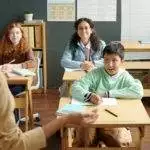 Happy multiethnic schoolboy and two schoolgirls looking at teacher