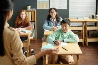 Happy multiethnic schoolboy and two schoolgirls looking at teacher